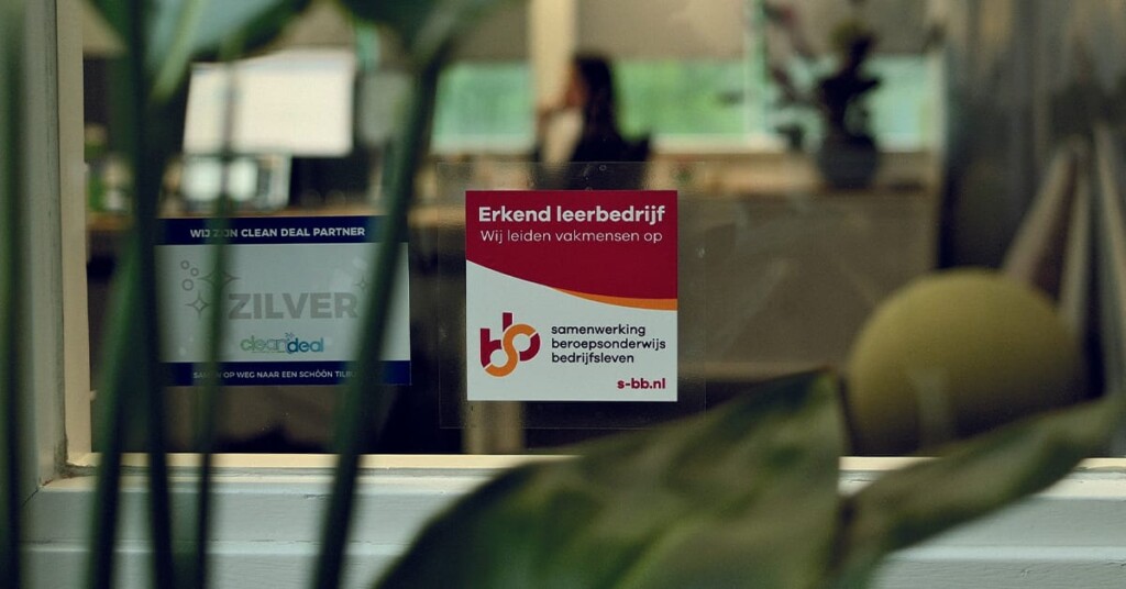 Sticker van erkend leerbedrijf op raam met planten op voorgrond